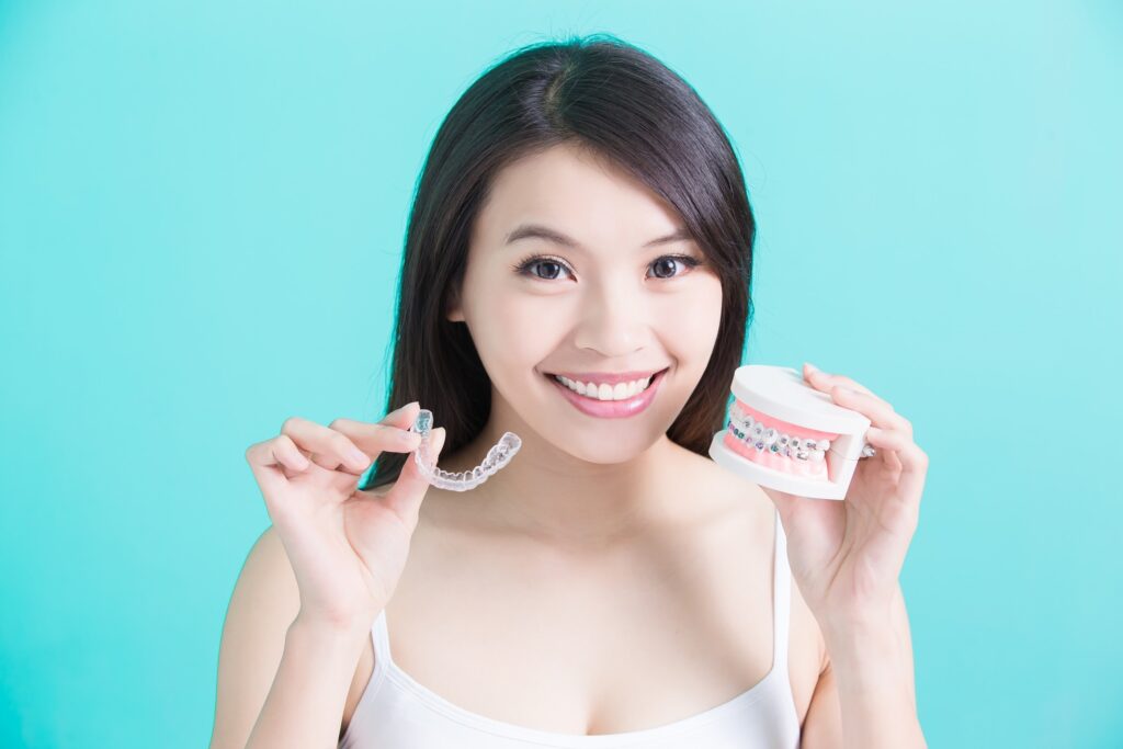 Woman holds Invisalign aligner and prosthetic teeth with metal braces to show the differences between the two