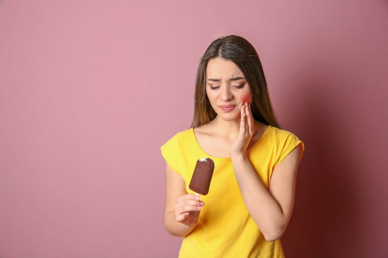 Woman touching her cheek and experiencing tooth pain after biting into an ice cream bar