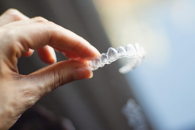 Woman holds up a clear tooth aligner, similar to Invisalign or ClearCorrect aligners